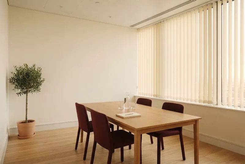 Uma pequena sala de reuniões luminosa com mesa de carvalho e cadeiras, luz da tarde